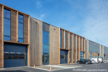 Bâtiment moderne de Blueprint Automation (PBA) de style bois avec plusieurs grandes fenêtres et portes de garage. Les voitures sont au premier plan, tandis qu'un ciel bleu est visible en arrière-plan.