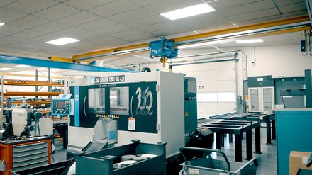 Un hall d'usine avec des machines-outils. Un pont roulant de type ELV avec palan électrique à câble roule sur un chemin de roulement.