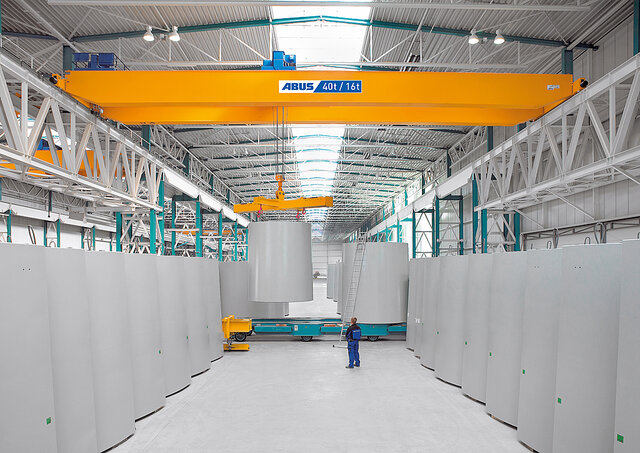 Un pont roulant déplace de lourdes charges dans un hangar industriel, tandis qu'un employé se trouve dans la zone d'action.