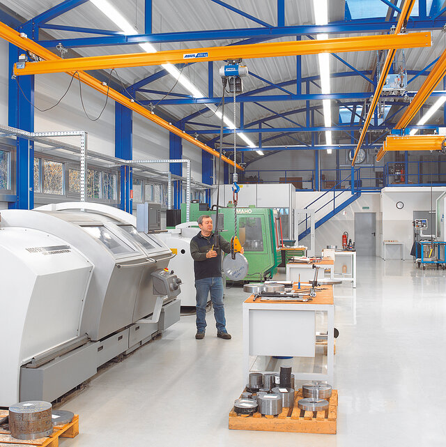 Un employé utilise un système de voie suspendue équipé d'un palan à chaîne et déplace une charge dans un atelier