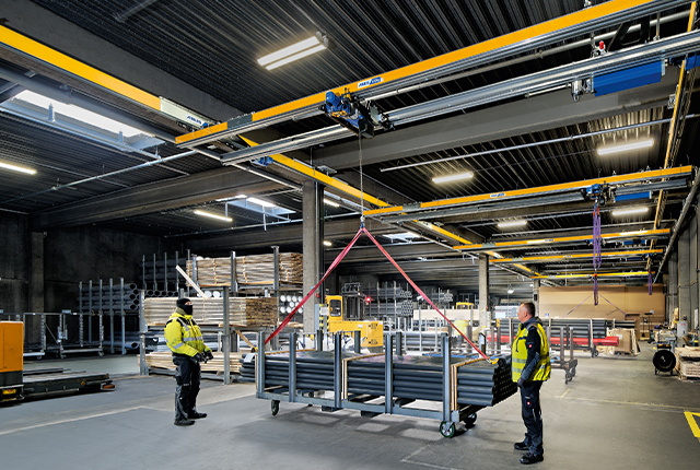 Un pont bipoutre ZHB effectue le levage d'une charge dans un hangar industriel, sous le regard des employés.