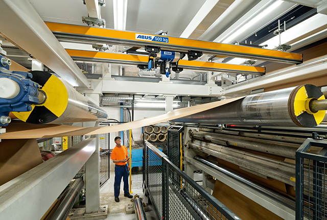 Un convoyeur à deux rails achemine les matériaux le long de la chaîne de production, tandis qu'un employé supervise le processus.